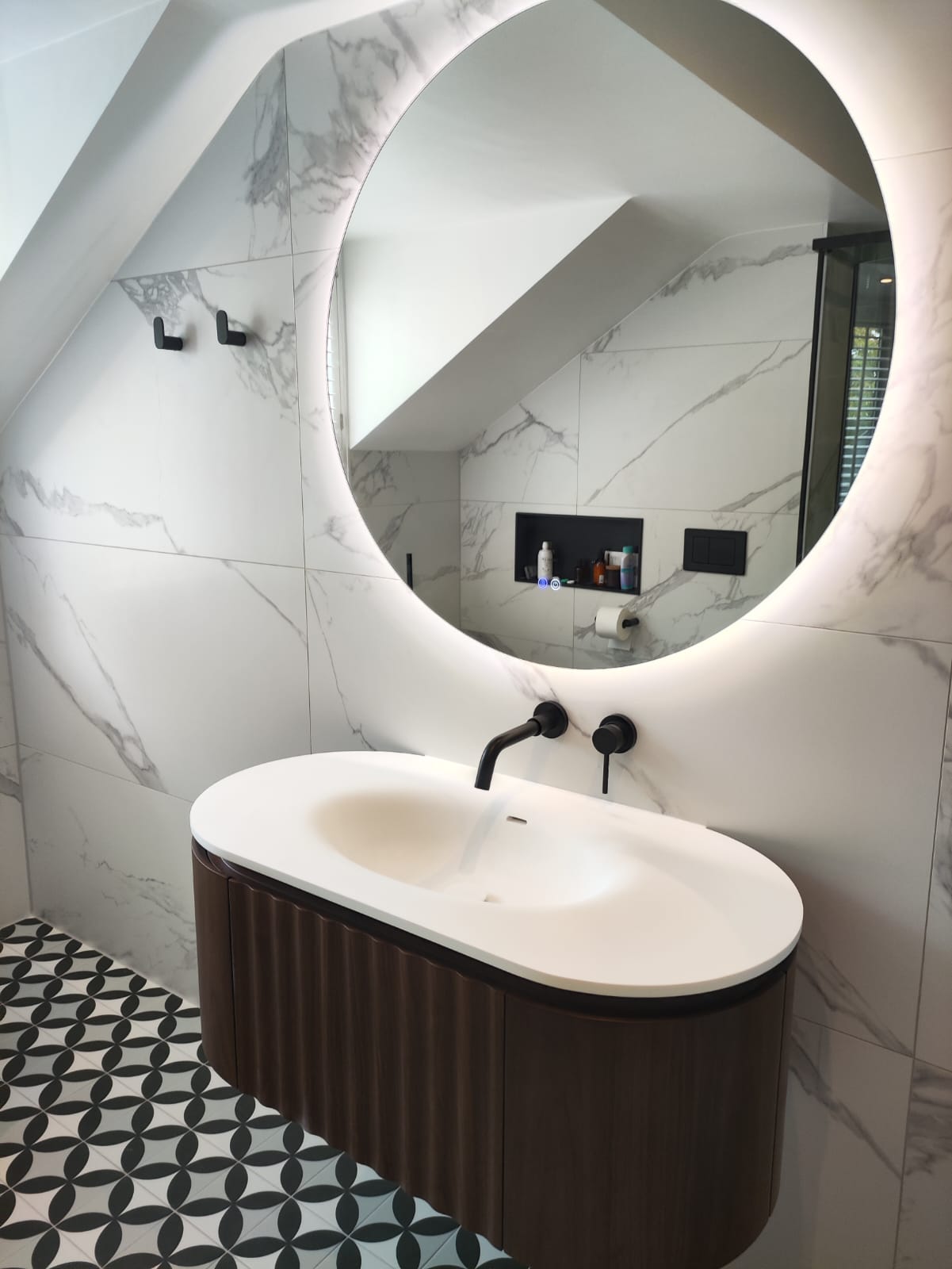 Marble bathroom with round backlit mirror and walnut vanity